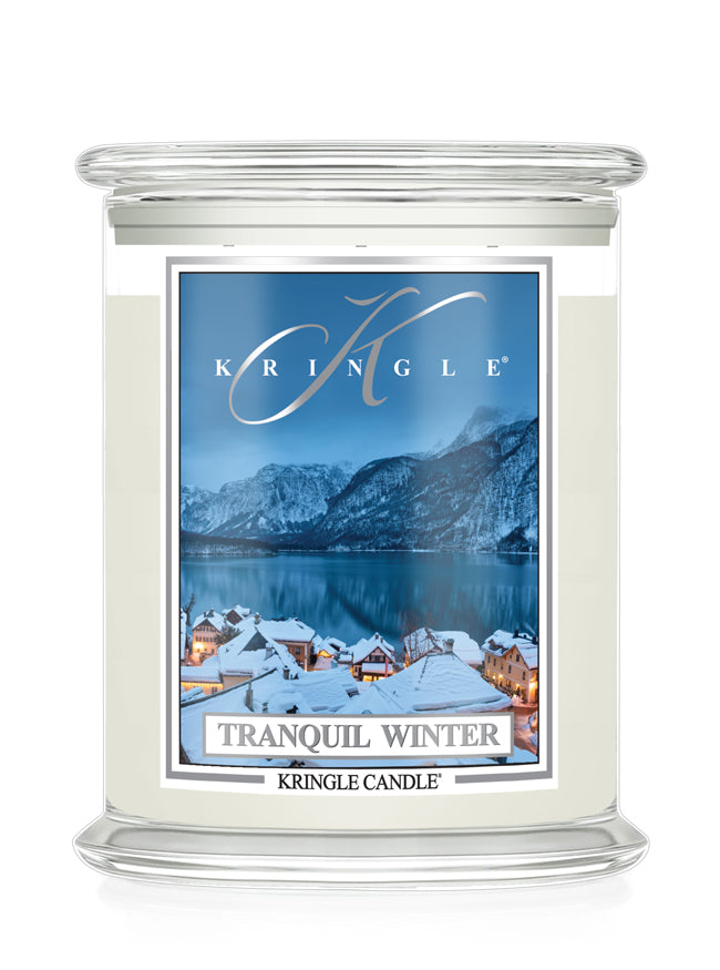 A Kringle Candle in a clear glass jar featuring a winter landscape label that reads 'Tranquil Winter' and shows snowy rooftops, mountains, and a blue lake.